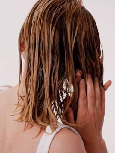 Osoba nakładająca produkt pielęgnacyjny na mokre włosy.