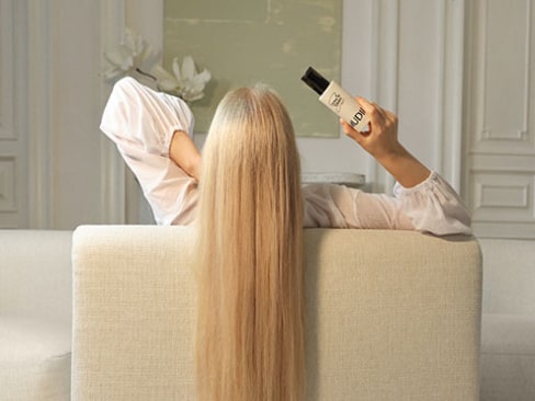 Kobieta z długimi, blond włosami trzymająca produkt Mudii do pielęgnacji włosów.